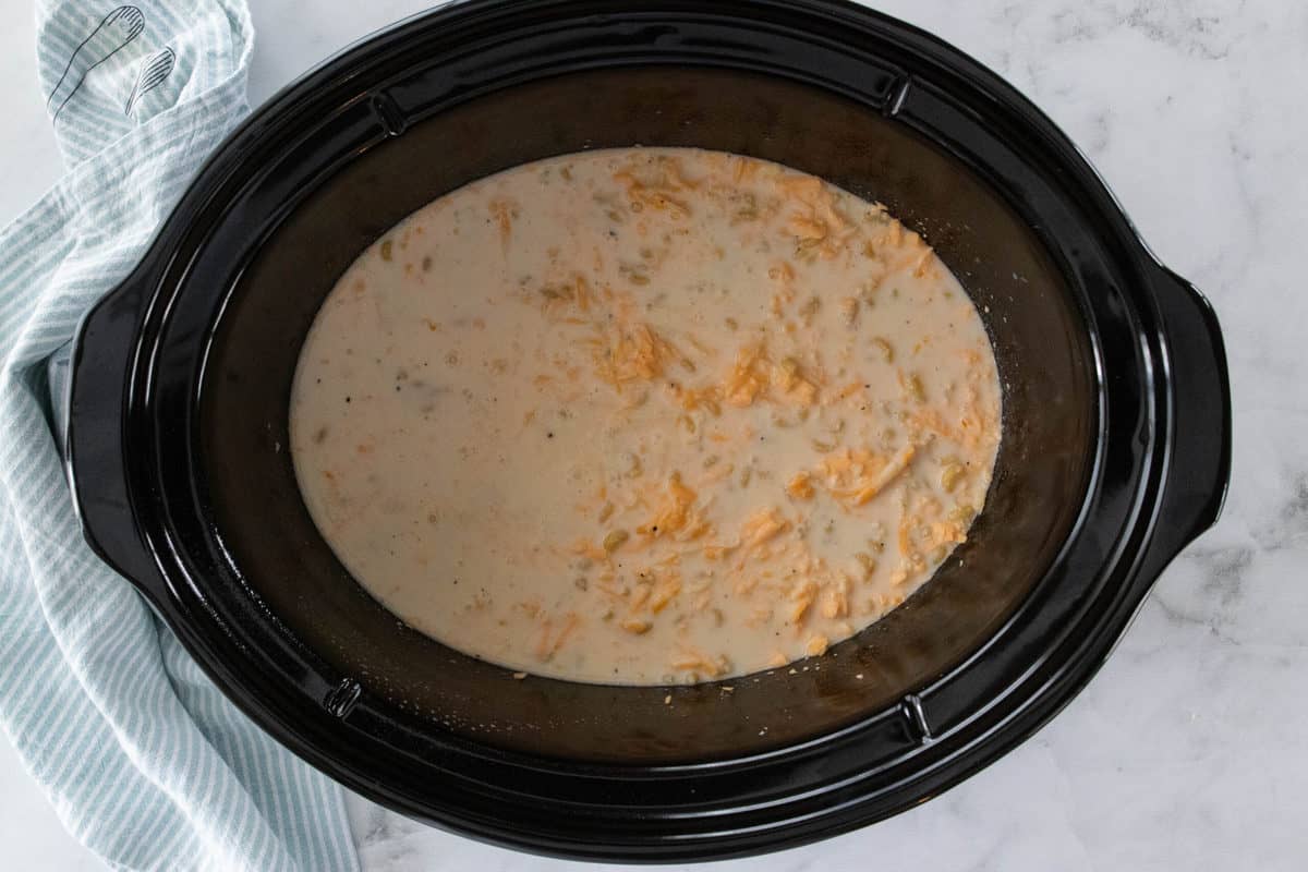 A crockpot insert shown filled with ingredients for Mac and cheese.