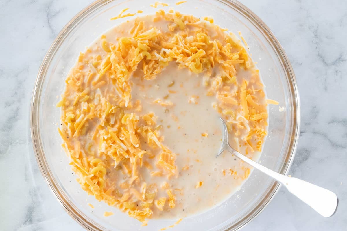 Ingredients for Crock Pot Mac n Cheese being shown in a large glass mixing bowl with a spoon in the bowl.