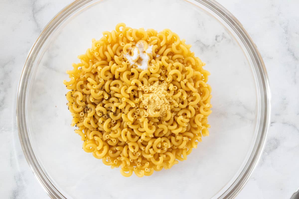 Macaroni with seasonings being shown in a large glass mixing bowl.