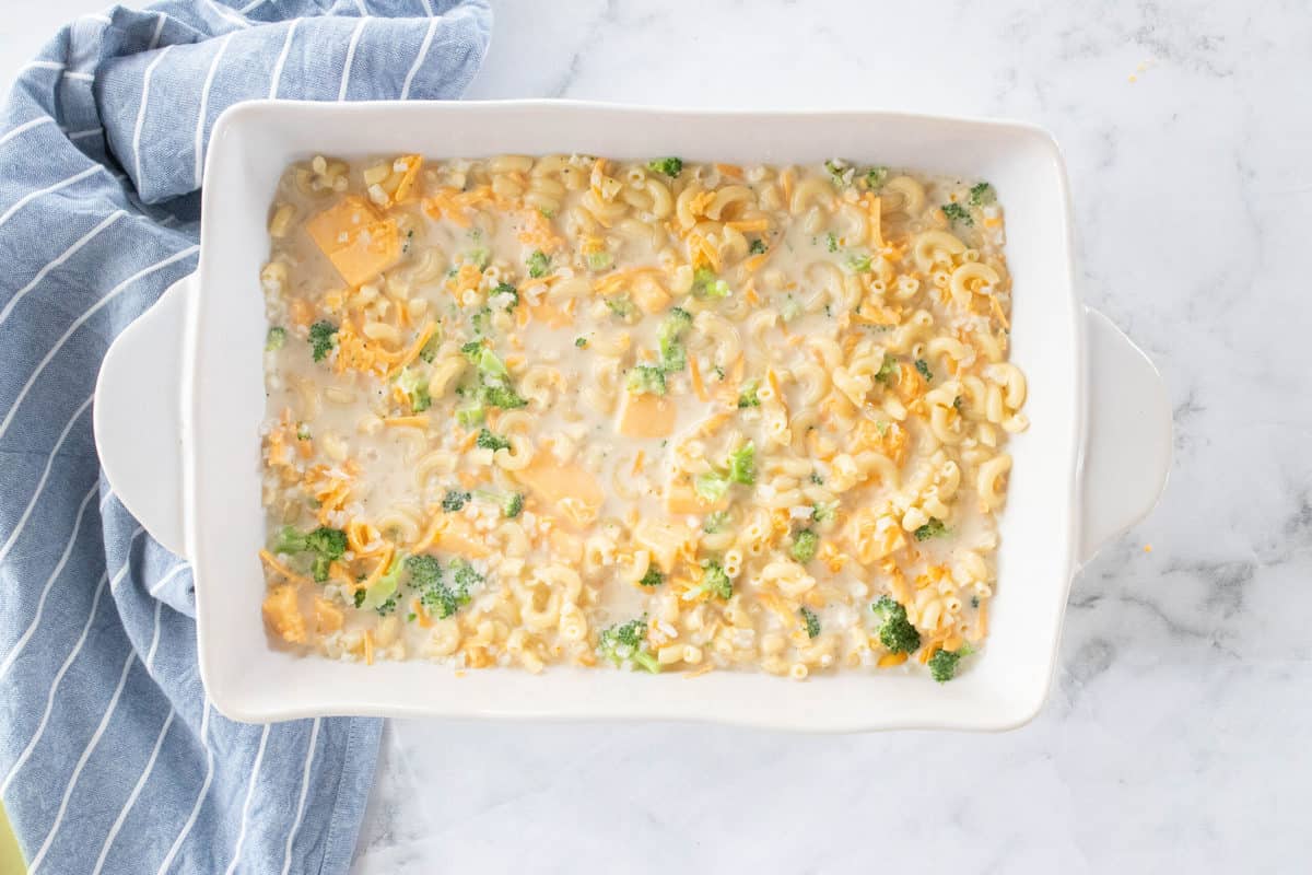 A large white baking dish filled with Mac n cheese on top of a granite countertop with a blue dish towel next to the dish. 