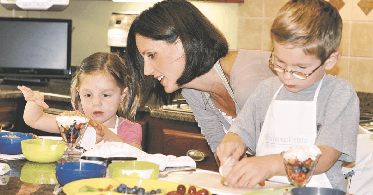 A parent and two preschoolers making yogurt parfaits.