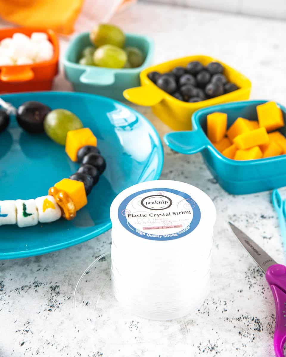 A preschool snack necklace on a plate with various ingredients and elastic string surrounding the plate. 