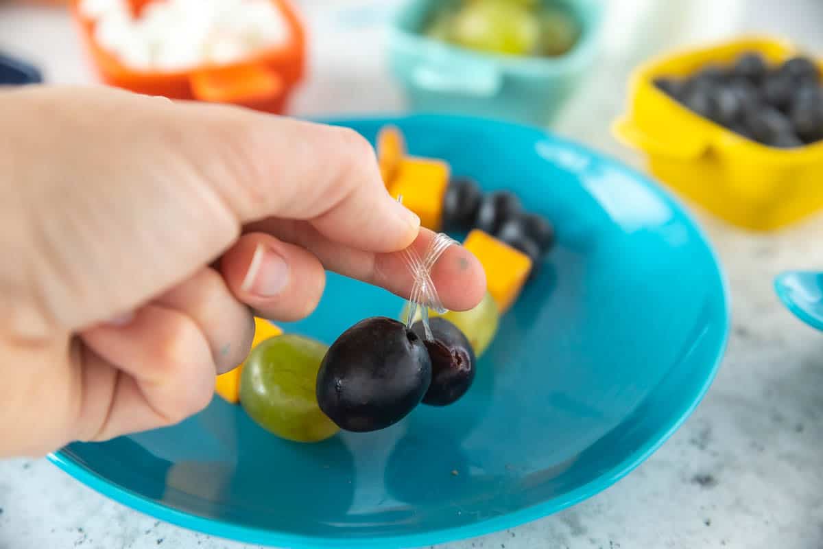 A snack necklace on a plate with a hand tying a knot.