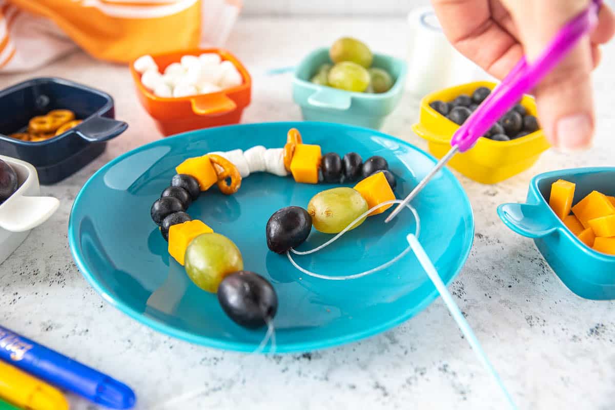 A preschool snack necklace on a plate with scissors cutting the string.