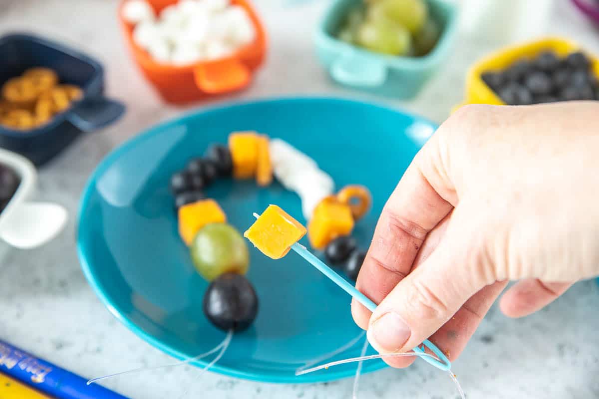 A snack necklace with cheese being threaded onto the string. 