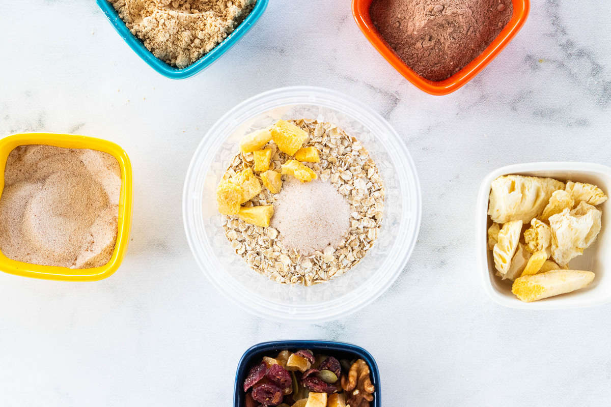 A container of oats surrounded by a variety of toppings 