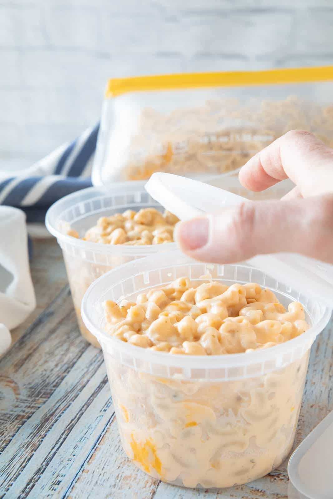 A hand placing a lid on top of a plastic container of Mac & cheese.