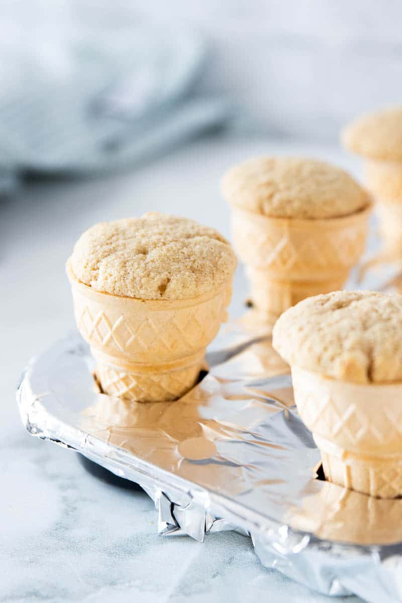 A tinfoil lined muffin tin being shown with an ice cream cone cupcake in each tin.