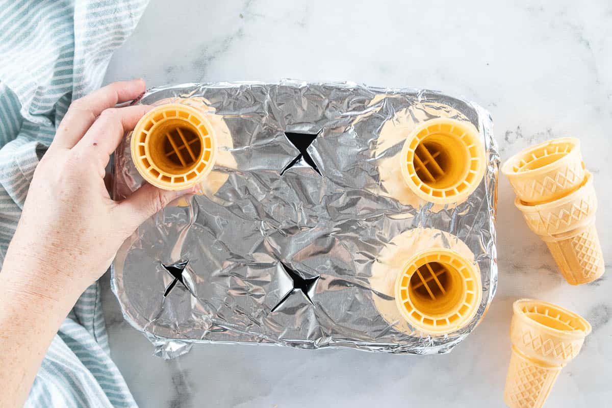 Ice cream cones being placed in a tinfoil lined muffin tin. 