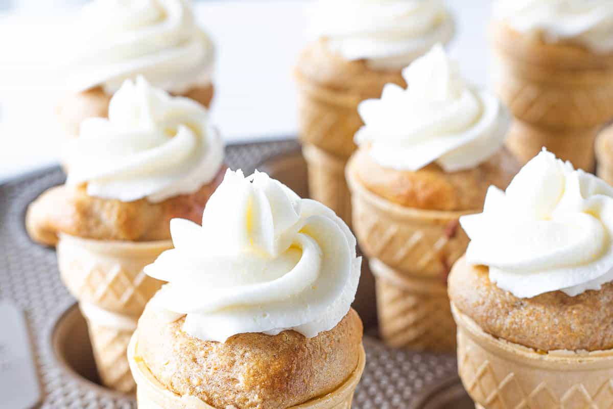 Ice cream cone cupcakes topped with almond buttercream frosting being shown in a muffin tin.