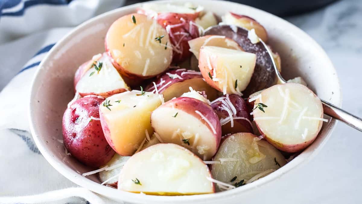 Red potatoes topped with herbs and parmesan cheese in a bowl with a spoon.