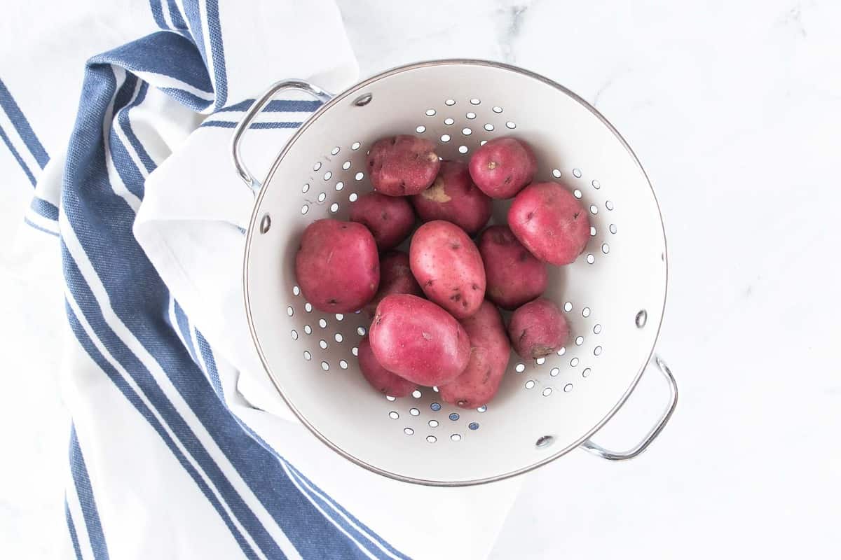 Whole red potatoes in a strainer.