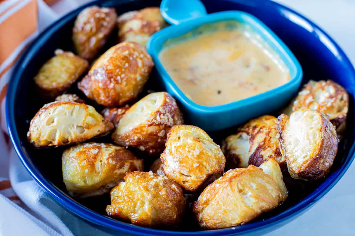 Pretzel bites being shown in a large serving bowl with a small dish of cheese sauce in the serving bowl. 