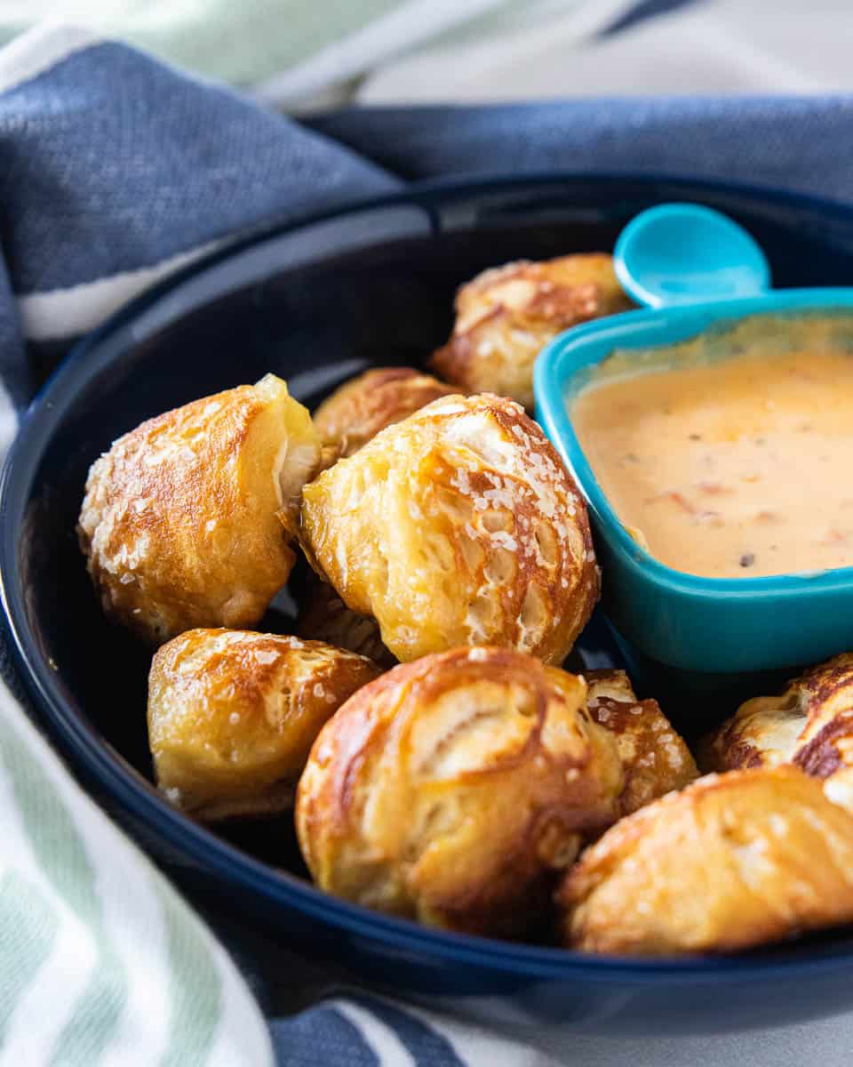 Soft pretzel bites being shown in a serving bowl with a small dish of cheese sauce next to the bites. 