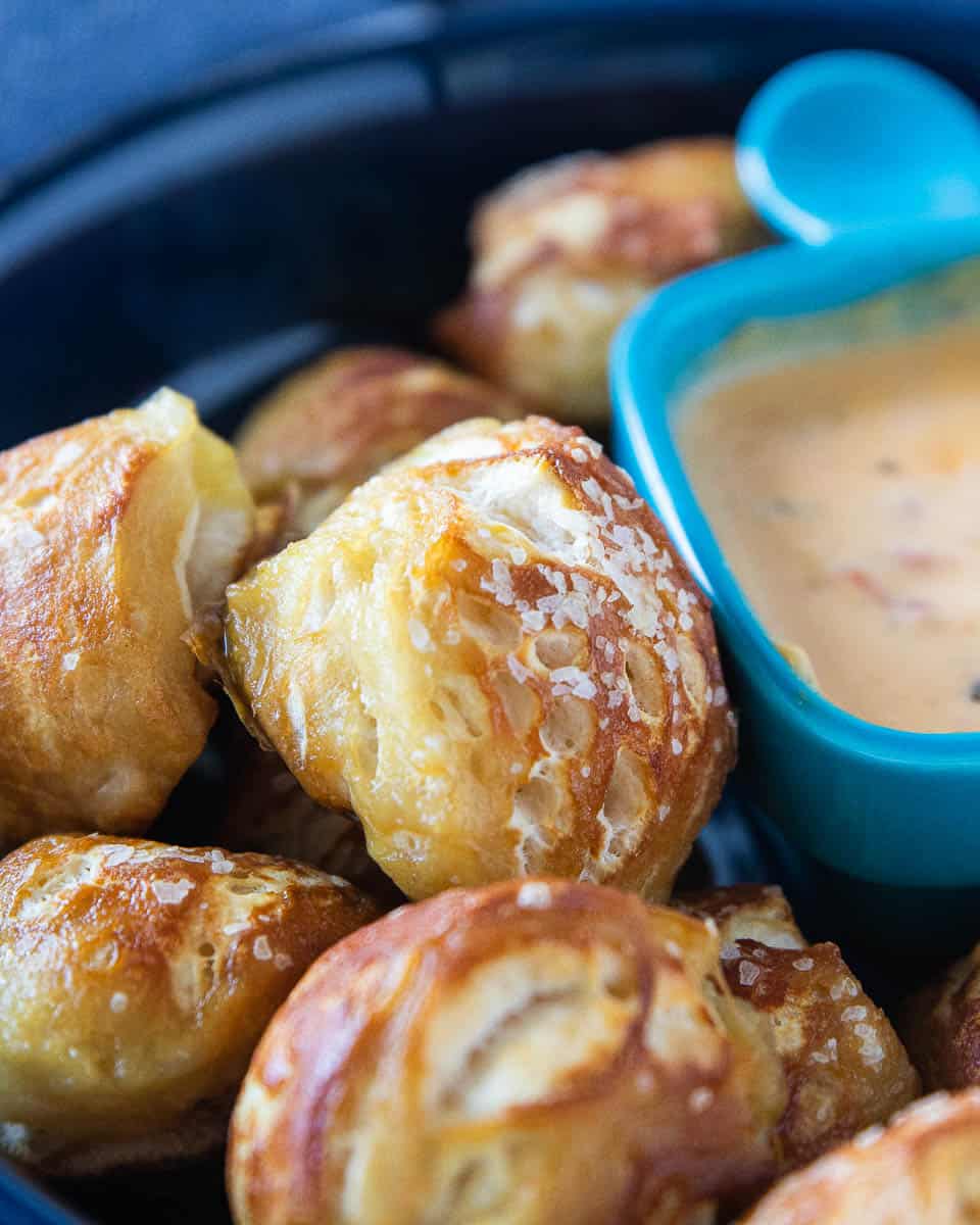 Pretzel bites and a small dish of cheese sauce being shown in a large serving bowl.