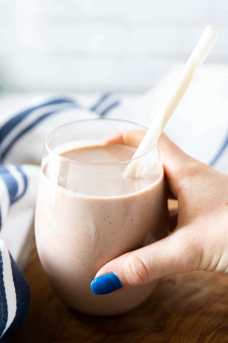 A child's hand holding a chocolate protein shake in a glass with a straw. 