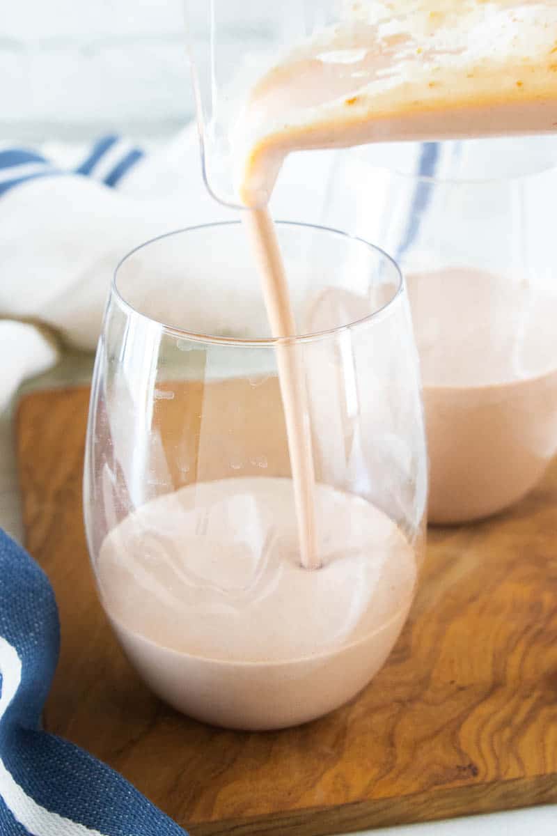 A chocolate protein shake being poured into a drinking glass next to another full glass of the shake. 