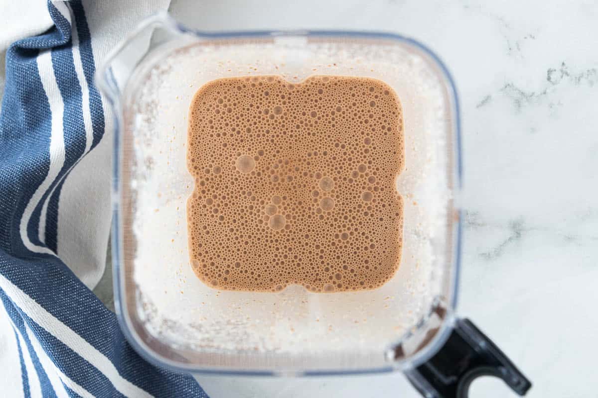 Ingredients for a kids protein shake blended together in a blender that is on top of a countertop with a dish towel next to the blender. 