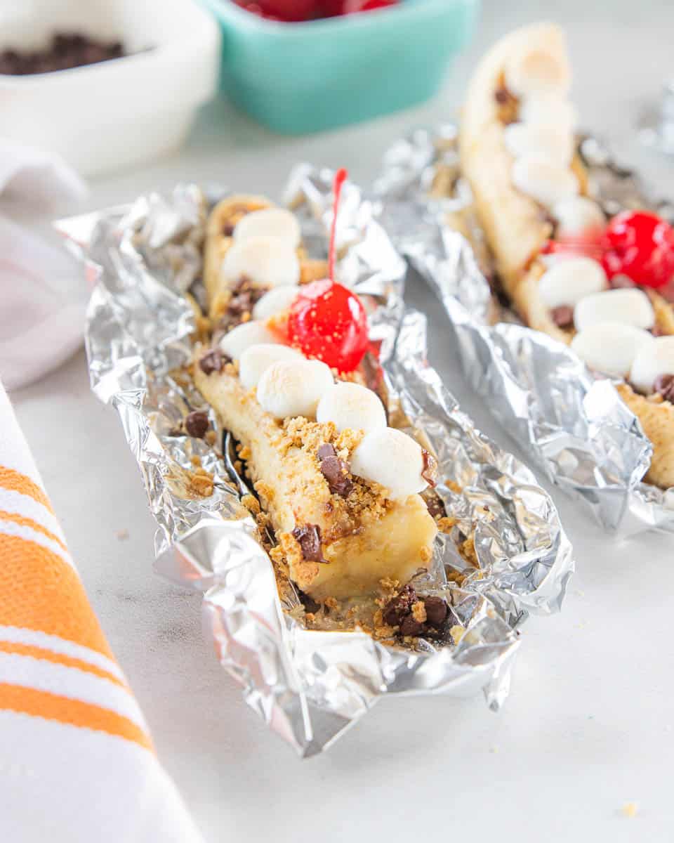 A banana dessert being shown in top with marshmallows, chocolate chips, graham crackers and a cherry on top of the banana. 