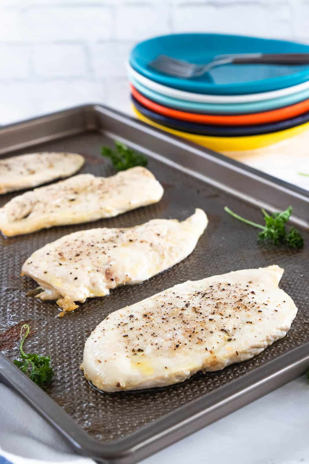 Thin sliced chicken breasts being shown on a baking sheet.