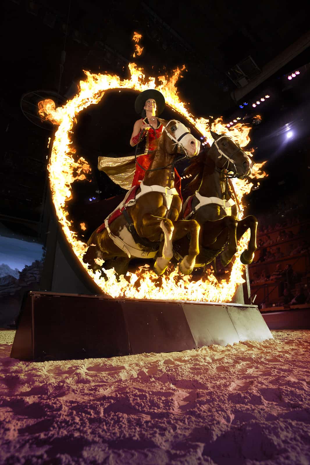 women on two horses jumping through a ring of fire