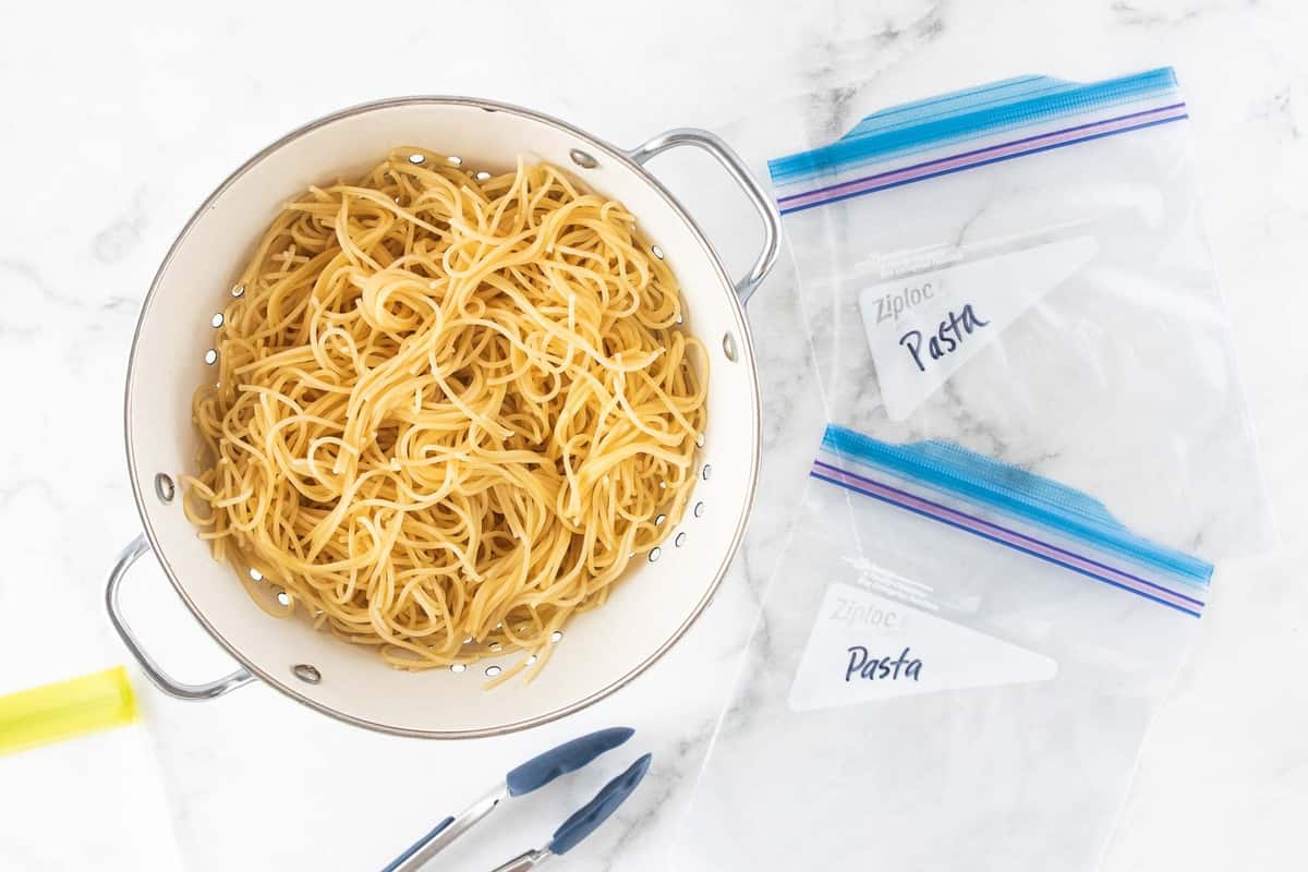 cooked pasta in strainer next to plastic bags.