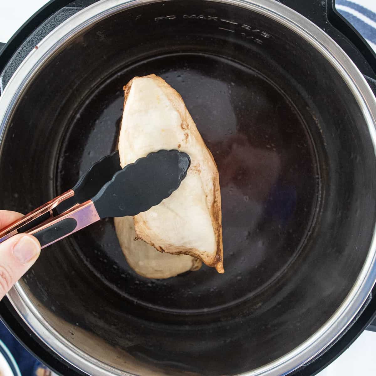 A pair of tongs placing a chicken breast in an instant pot.