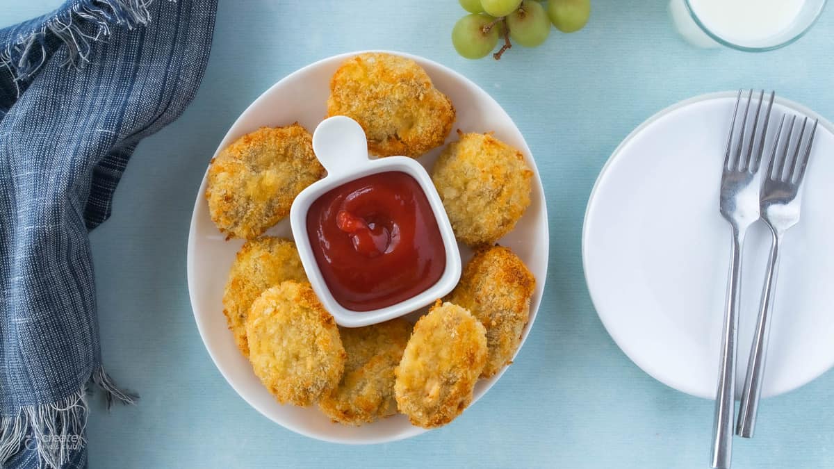 homemade chicken nuggets on a plate next to ketchup. 