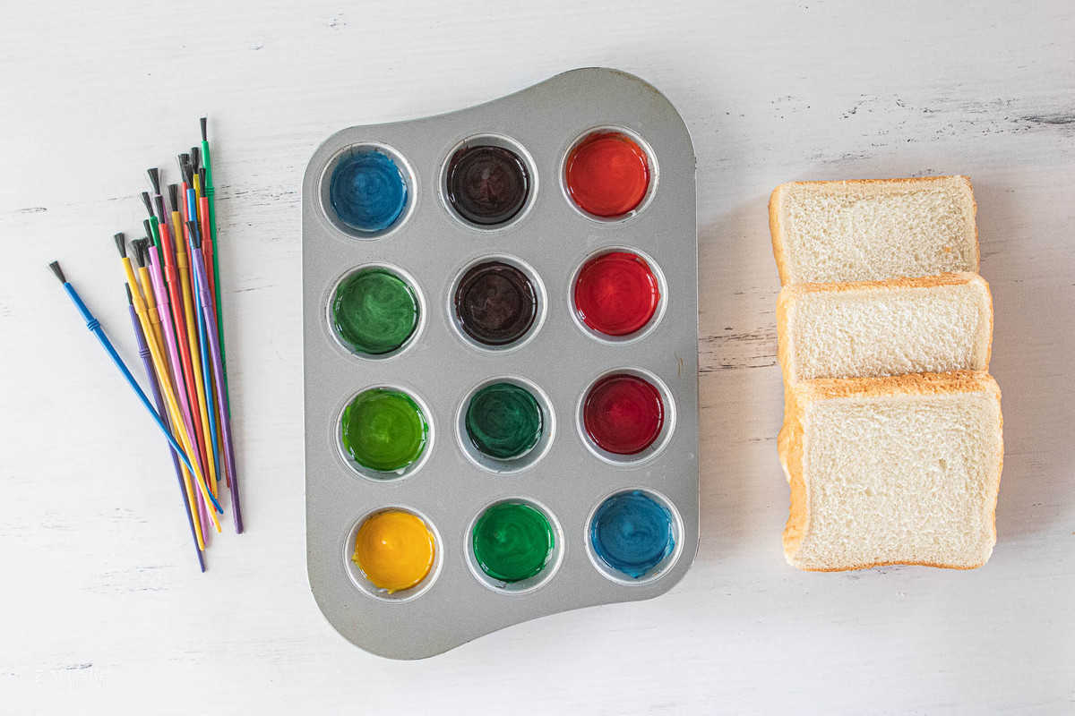 paint colors in a muffin tin with slices of bread and paint brushes next to the tin