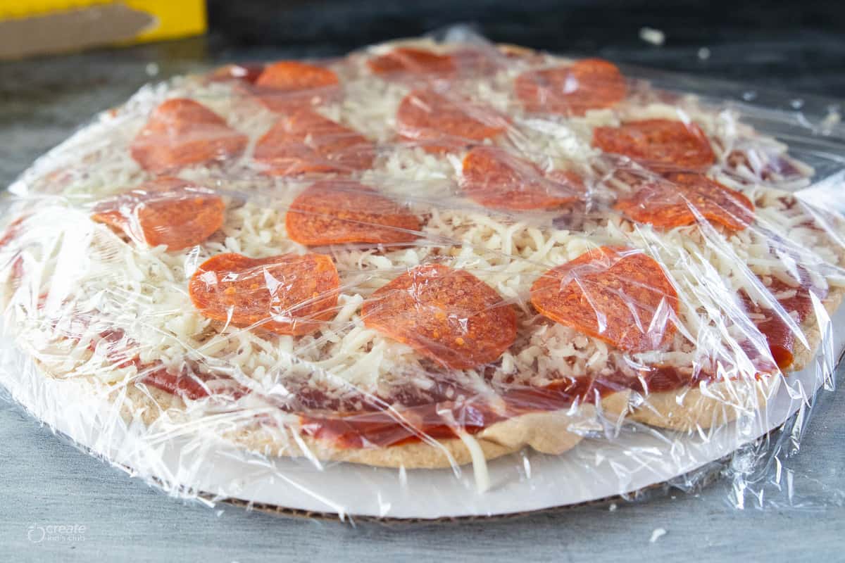 pepperoni pizza on cardboard round covered with plastic wrap