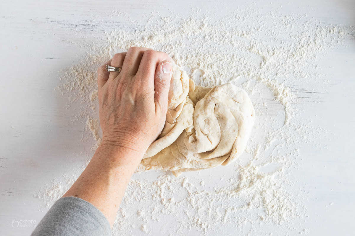 hand kneading bread dough on floured surface