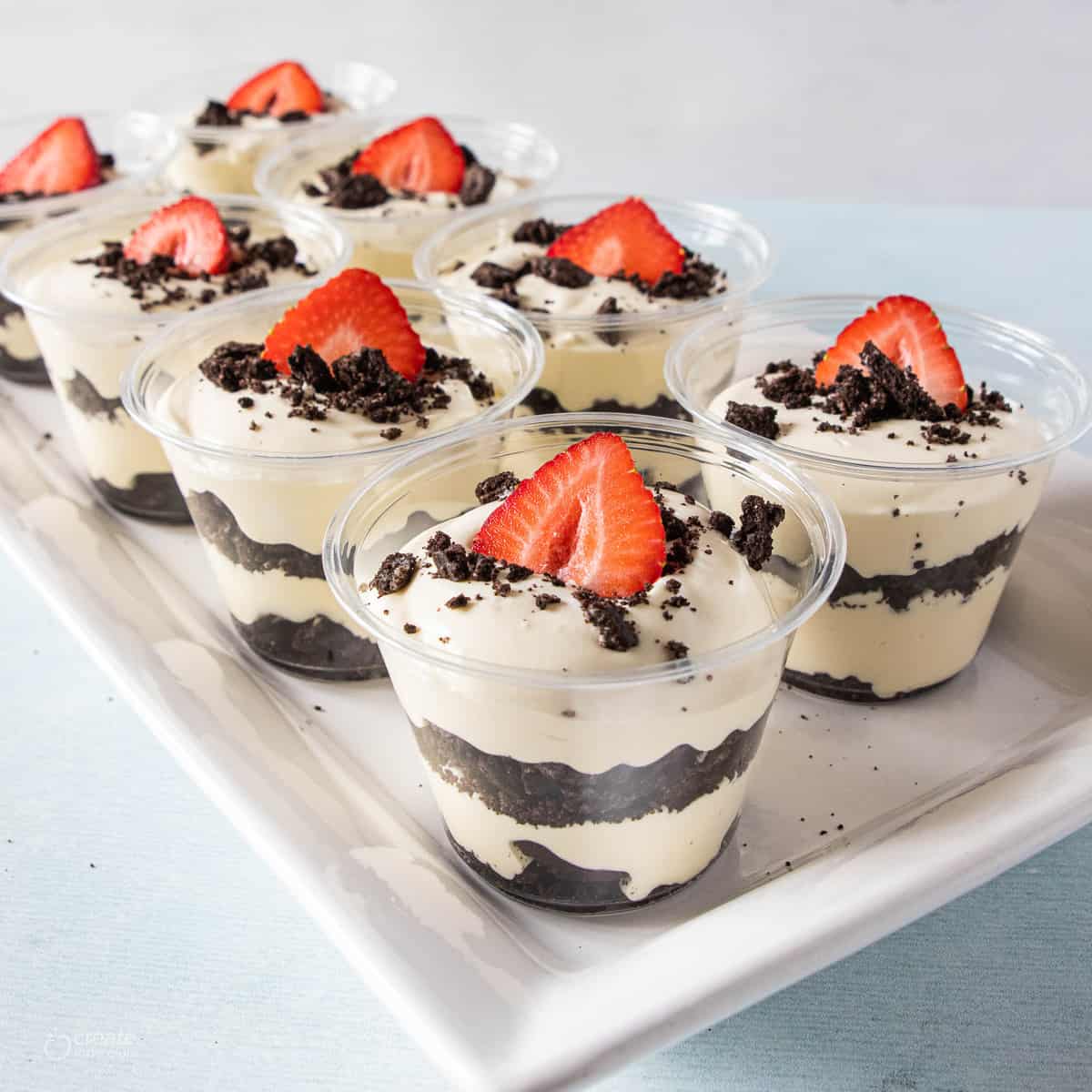 layers of crumbled oreos and pudding in cups topped with a strawberry slice