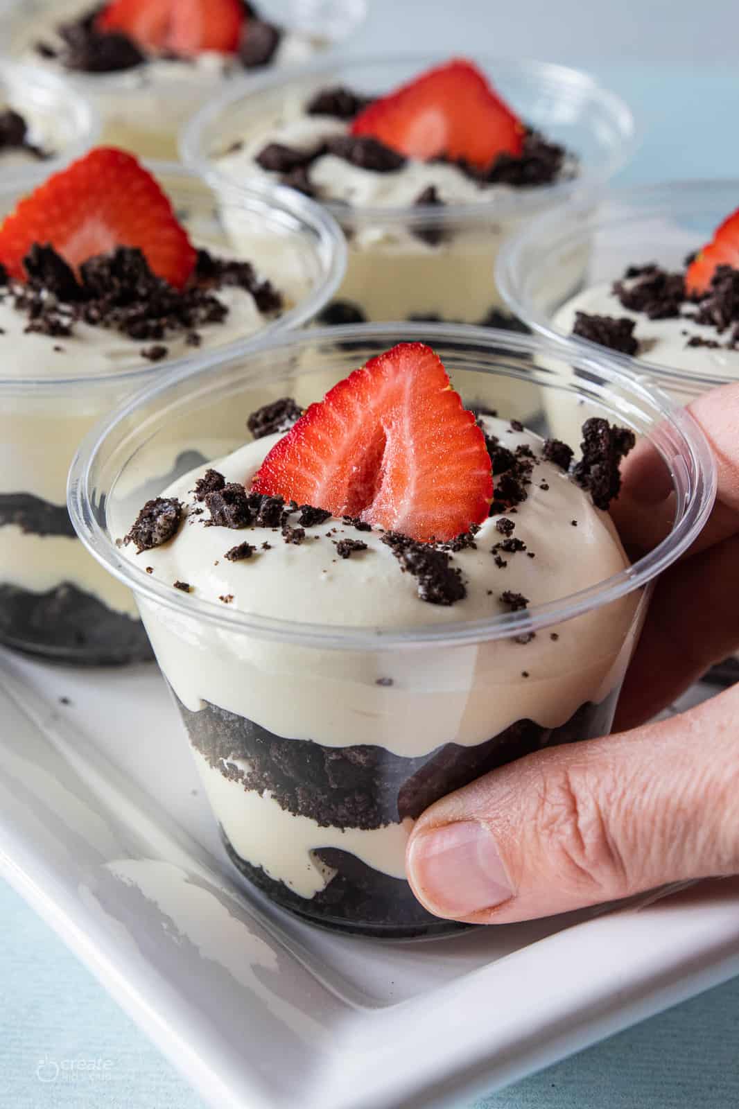 layers of crumbled oreos and pudding in cups topped with a strawberry slice