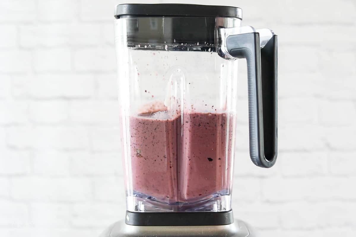 A blueberry and spinach smoothie shown being blended in a high speed blender.