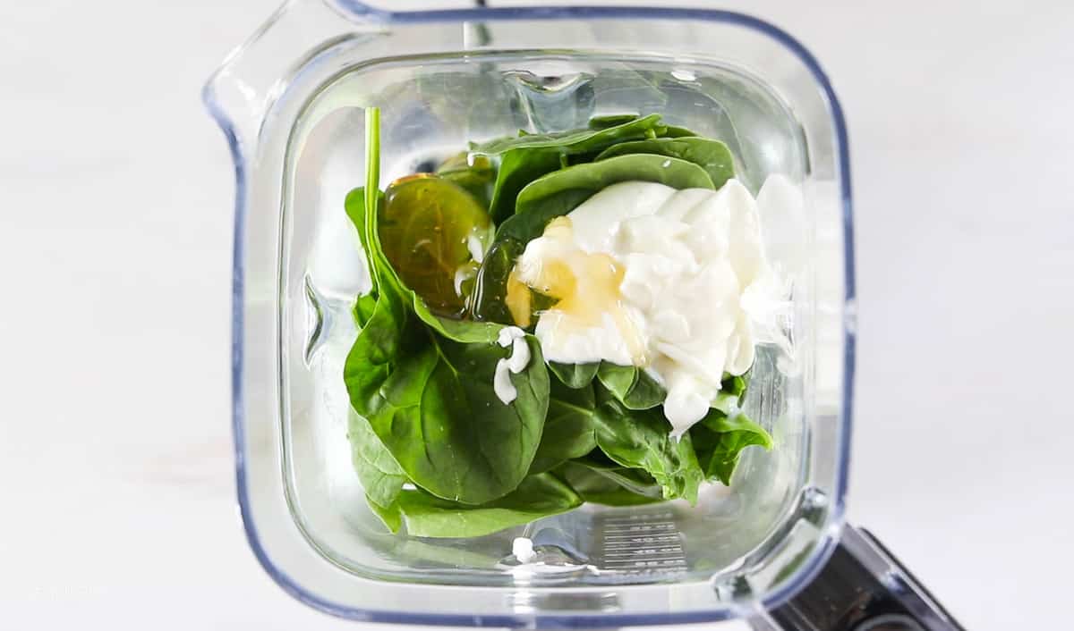 A top down view into a blender showing spinach, yogurt, and honey.