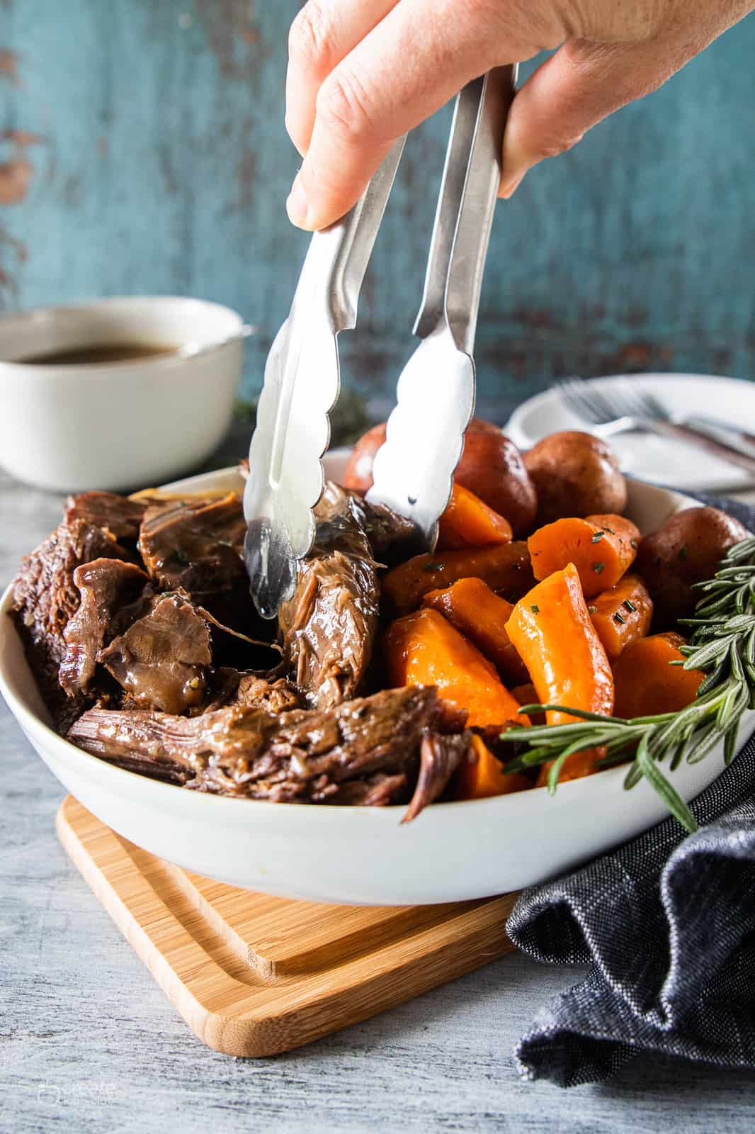 tongs picking up pot roast from serving bowl
