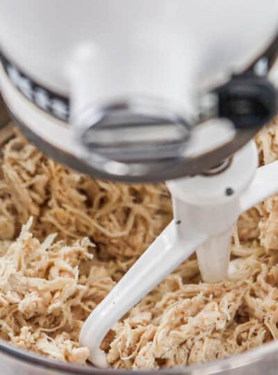 A close up of shredded chicken in a kitchenaid mixer being shredded.