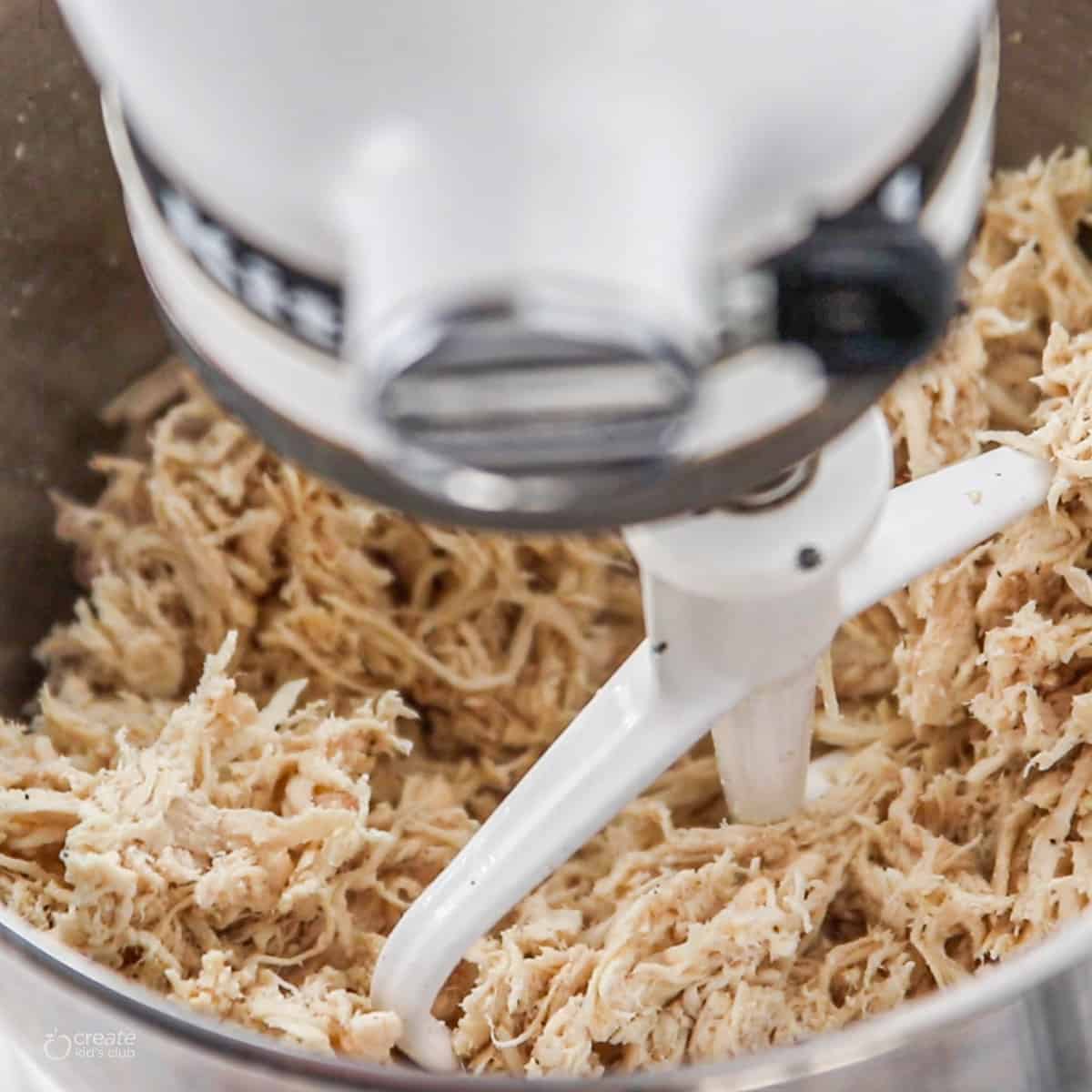 A close up of shredded chicken in a kitchenaid mixer being shredded.