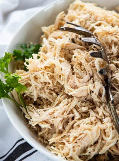 Shredded chicken in a white bowl with a spoon in the bowl.