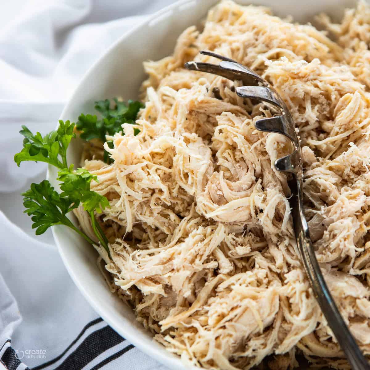 Shredded chicken in a white bowl with a spoon in the bowl.