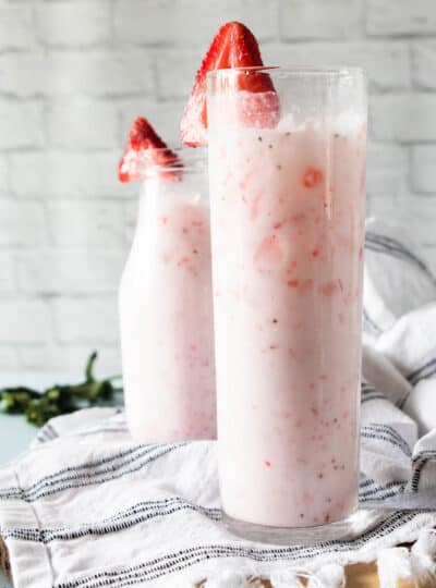 Two tall glasses filled with a pink drink with a kitchen towel underneath.