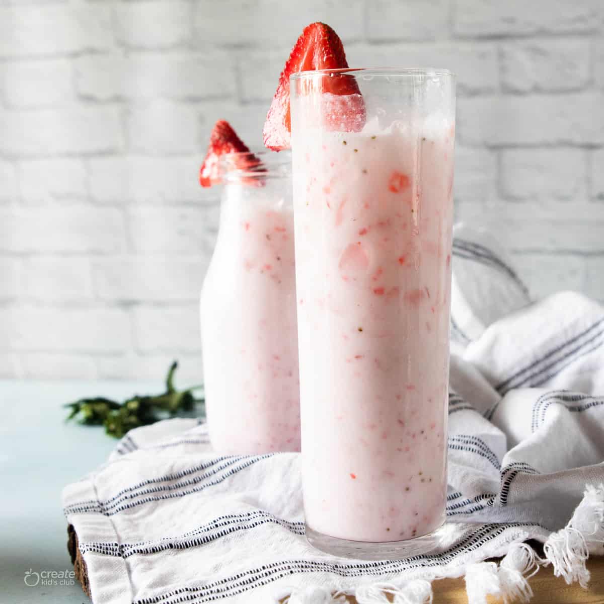 Two tall glasses filled with a pink drink with a kitchen towel underneath.