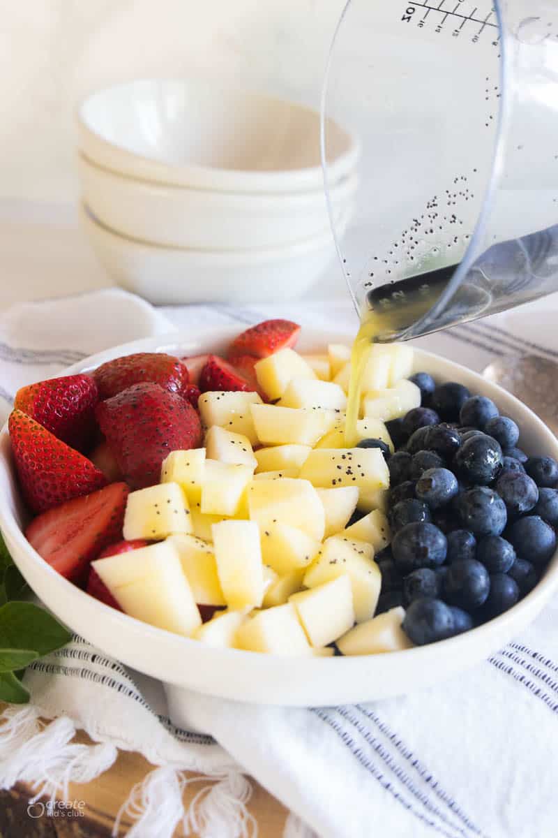 Dressing being poured onto a red, white, and blue fruit salad.