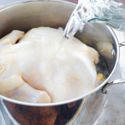 water poured over whole chicken in a pot