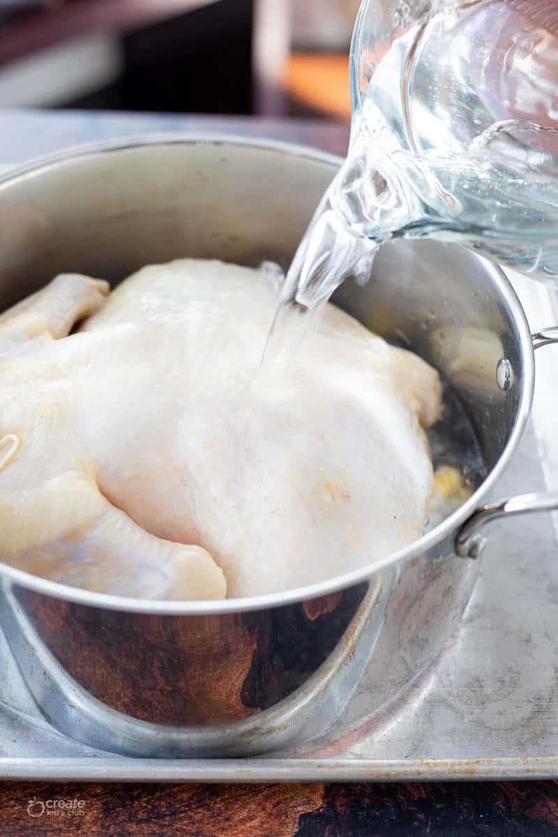 water poured over whole chicken in a pot