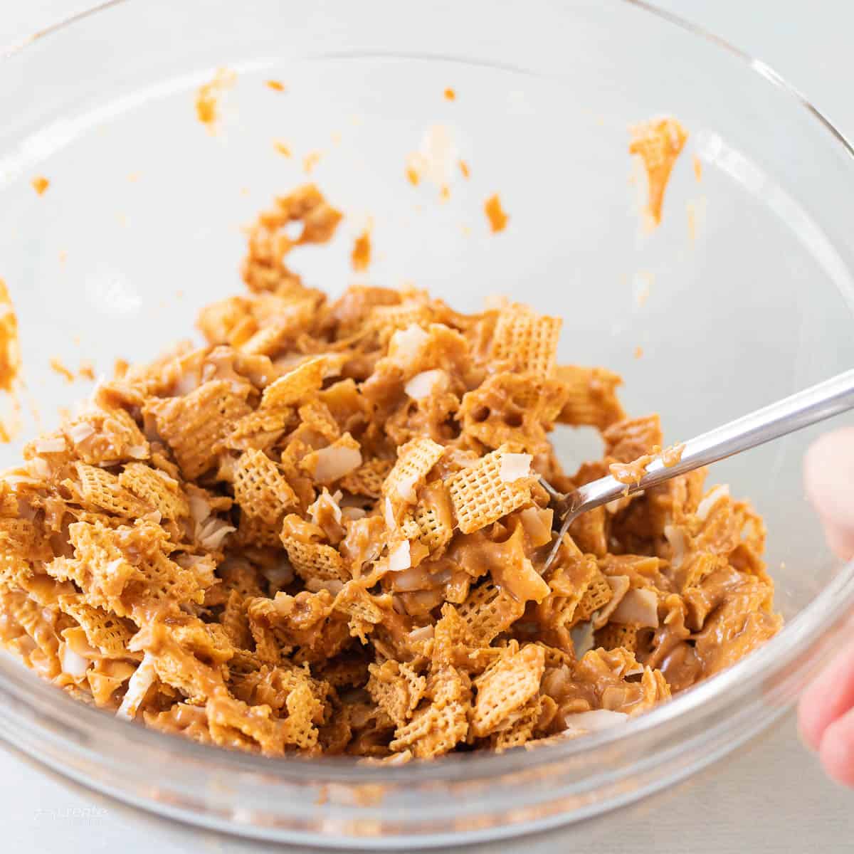 Chex cereal, peanut butter and coconut shreds stirred together in bowl