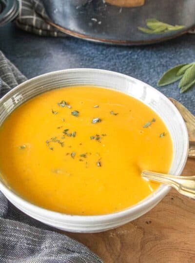 A close up shot of butternut squash and sweet potato soup in a white bowl.