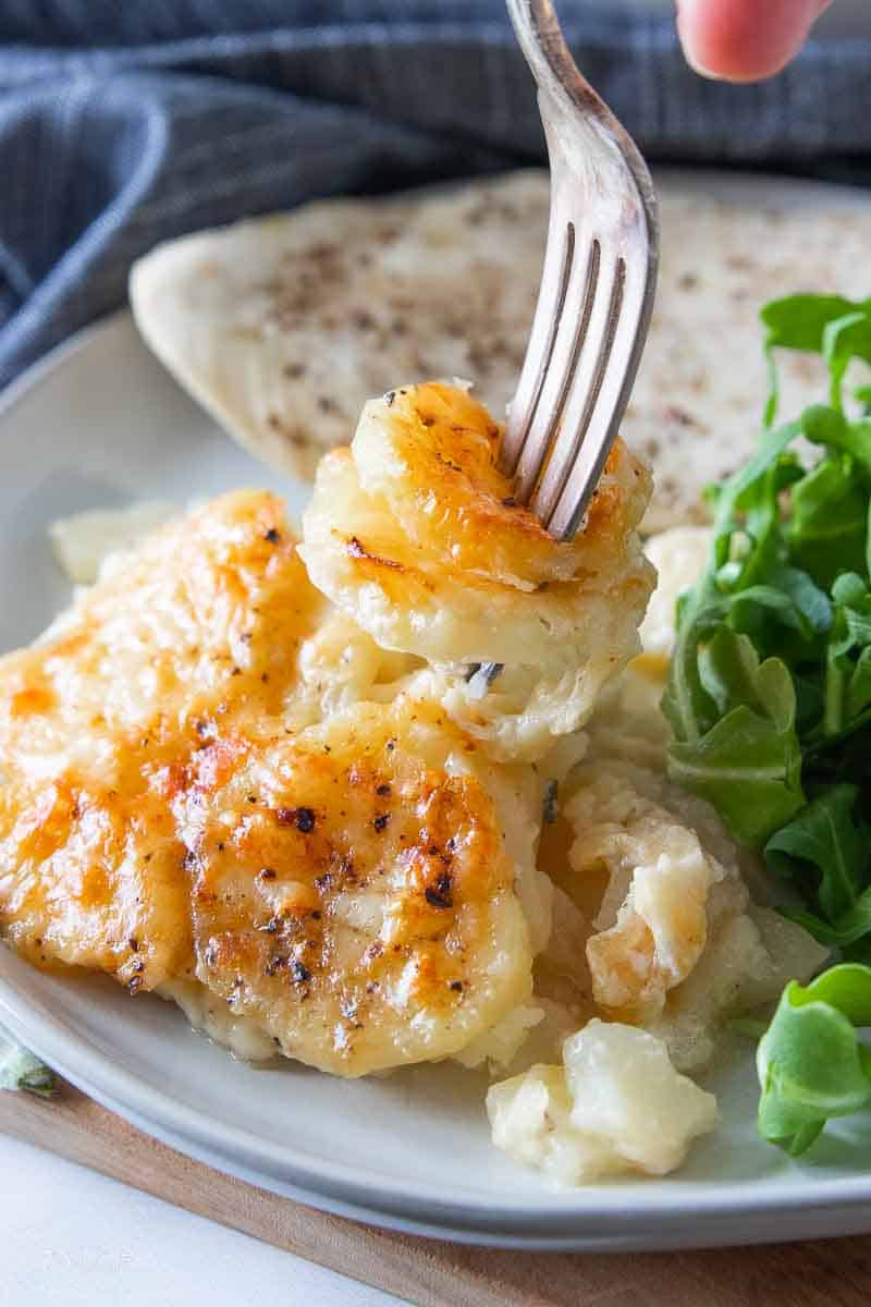 fork scooping bite of scalloped potatoes from plate