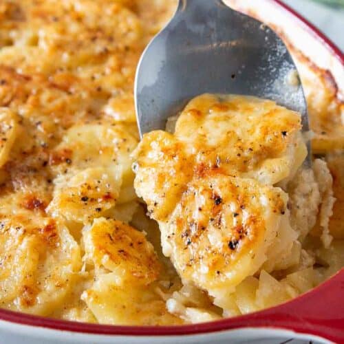 spoon serving scalloped potatoes from baking dish