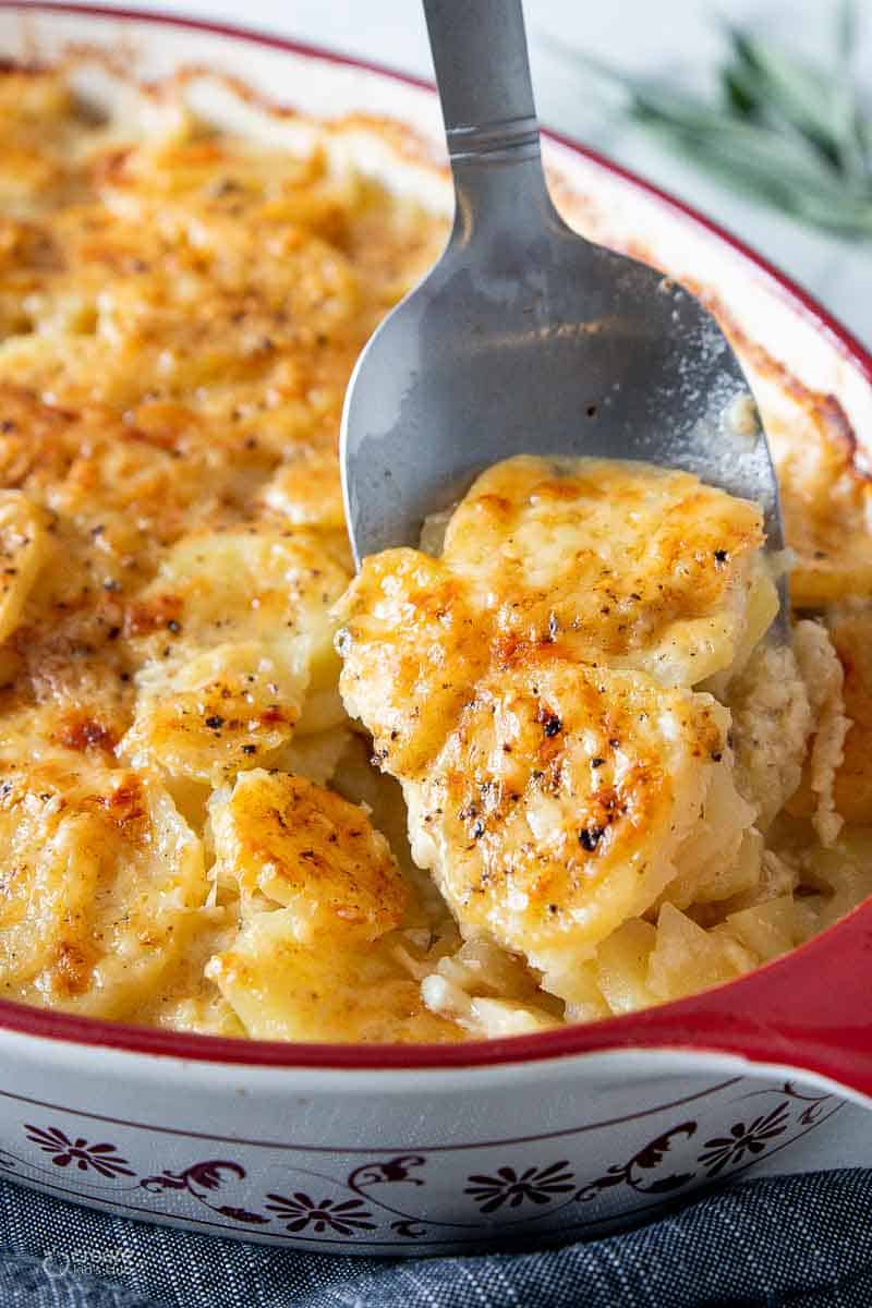 spoon serving scalloped potatoes from baking dish